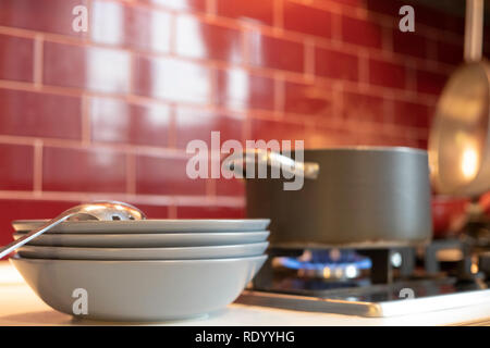 grey cooking pot on gas stove with steam releasing and blue dishes on the side in red burgundy classic kitchen. Stock Photo