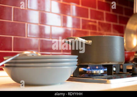 grey cooking pot on gas stove with steam releasing and blue dishes on the side in red burgundy classic kitchen. Close up. Stock Photo