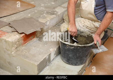 The construction worker evenly spreads the surface of the stairs with cement adhesive mass using a special hand tool. Stock Photo