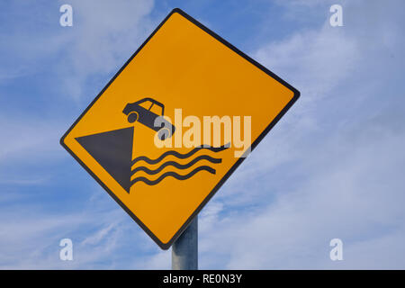 Sign Caution Car falling from Pier.  Diamond shape, yellow background on an angle against blue and clouds Stock Photo
