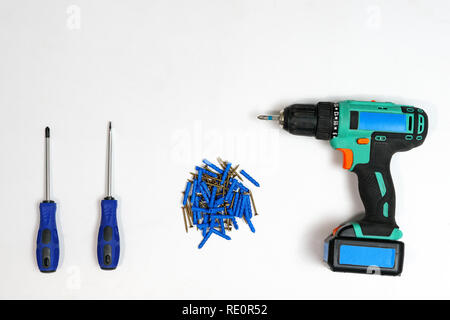 Top view of arranged drill with screwdrivers and pile of nails on white background Stock Photo