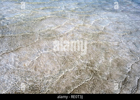 Empty background with natural textured pattern created by small sea waves in shallow waters of golden sand beach. Water surface is shining because of  Stock Photo
