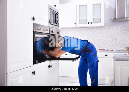 Mature Technician In Overall Repairing Oven In Kitchen Stock Photo