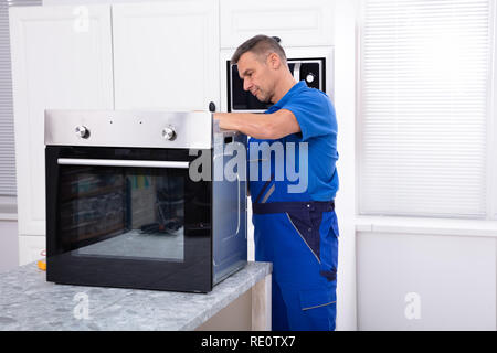 Mature Male Technician Repairing Oven On Kitchen Worktop Stock Photo
