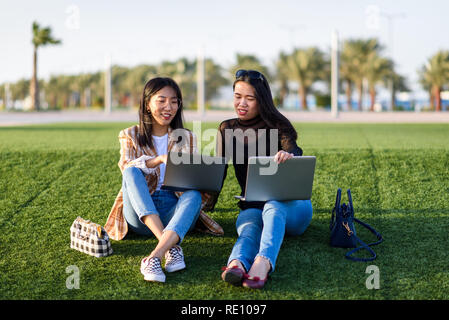 Two Asian girls working on laptop outdoors Stock Photo