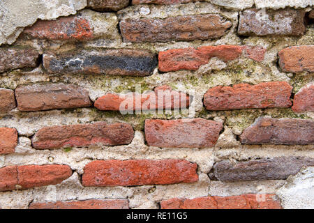 Old brick wall covered in concrete, weather worn concrete layer has crumbled away revealing underlying brick. Decrepit condition. Stock Photo