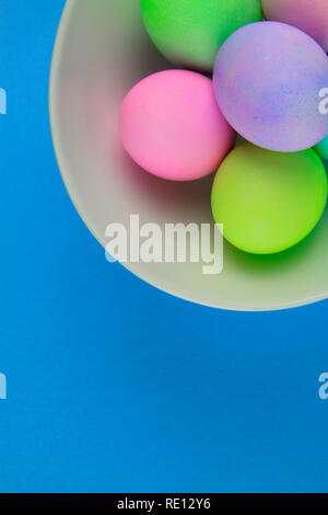 Overhead view of brightly painted easter eggs in a white bowl on blue background Stock Photo