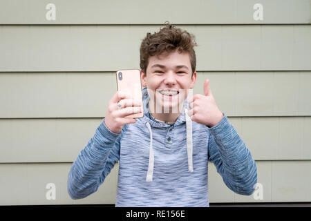 Male teenager giving thumbs up while holding his new Apple iPhone X Stock Photo
