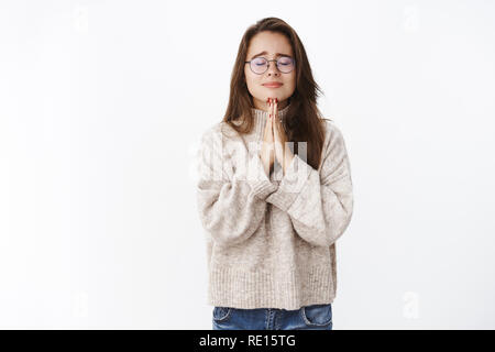 Girl feeling worried and insecure frowning being emotional as close eyes holding hands in pray, making wish praying faithfully with hope things get be Stock Photo