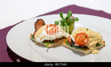 Beautiful benedict eggs with bacon, mustard sauce, and salad on a French toast. Stock Photo