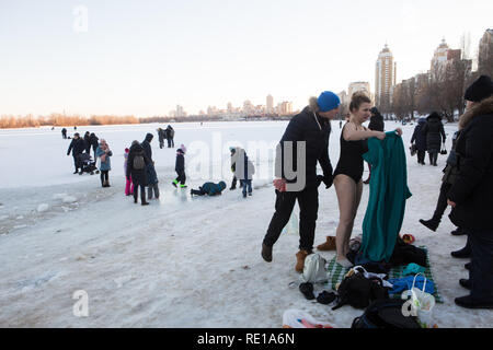 Ukrainian family on January morning prepares for a plunge into chilly water with young woman already in swimming suit and a man joking about wind Stock Photo