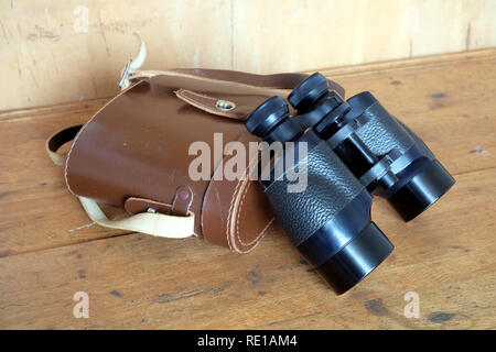Vintage Porro prism black color binoculars and closed brown hard leather carry case on wooden background side view indoor closeup Stock Photo