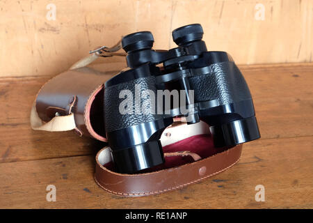 Vintage Porro prism black color binoculars and opened brown hard leather case on wooden background side view indoor closeup Stock Photo