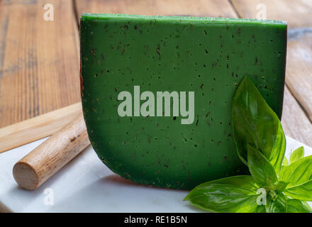 Cheese collection, piece of Dutch green pesto hard cheese with fresh basil close up Stock Photo