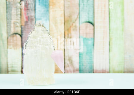Using crystal Selenite tower for loading rose quartz pendulum, light blue table and pastel color wooden board background. Divination, fortune telling Stock Photo