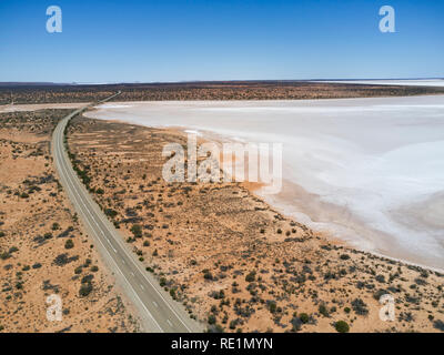 Aerial view of a highway running alongside a vast salt flat under clear blue sky in a desert landscape Stock Photo