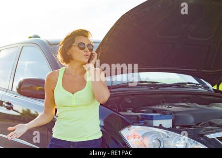 Frustrated woman driver near broken car. Car on country road, woman calls asking for help. Stock Photo