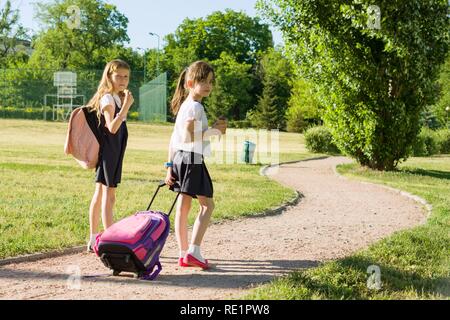 Rear view of two schoolgirl girlfriends elementary school students walking with school bag in the yard.