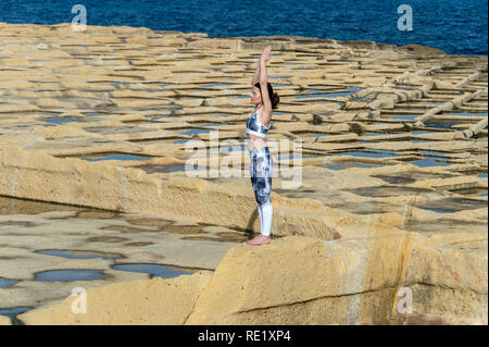 woman meditating, practicing the 'mountain pose' amongst the limestone salt pans in Malta Stock Photo