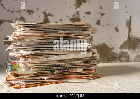 A stack of old newspapers on a table and a wall in a bad state of background Stock Photo