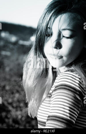 A tween girl looks down while displaying trendy dip dyed pink hair tips and crop top and jeans on balcony outside Stock Photo