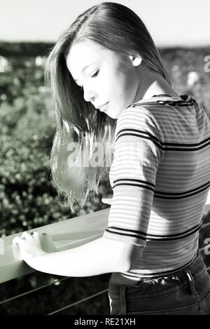 A tween girl looks down while displaying trendy dip dyed pink hair tips and crop top and jeans on balcony outside Stock Photo