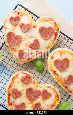 Mini pizzas - Fresh homemade heart shaped mini pizzas with pepperoni, cheese, tomatoes and basil. Overhead shot. Stock Photo