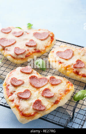Mini pizzas - Fresh homemade heart shaped mini pizzas with pepperoni, cheese, tomatoes and basil. Stock Photo