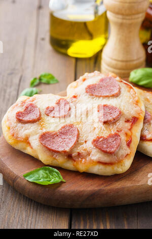 Baked heart shaped homemade pepperoni mini pizza on a wooden serving board. Romantic dinner concept. Stock Photo