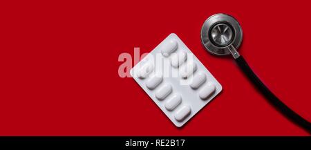 Stethoscope and medicine pills on red background. Panoramic picture with copy space. Stock Photo