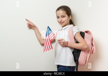 School child with a backpack holds the US flag, background bright wall in the school, Point with your finger location of copy space Stock Photo