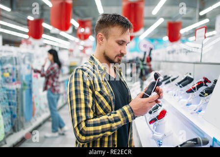 Man with electric shaving machine, couple in supermarket. Male and female customers on family shopping. Man and woman purchasing goods for the house Stock Photo