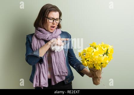 Spring allergy to pollen. Woman with bouquet of yellow flowers is going to sneeze. Background green matte wall Stock Photo