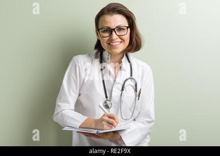 Smiling medical doctor woman with stethoscope taking notes on her notepad against green background Stock Photo