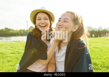 Young girls having fun sitting on green grass lawn. Background nature, recreation area, river Stock Photo