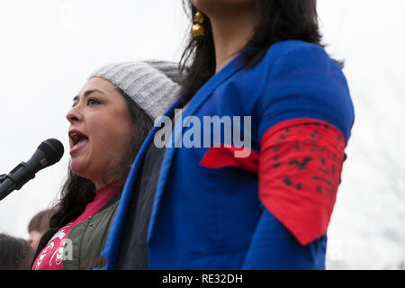 Washington, USA. 19th Jan 2019.  Colleen Echohawk, member of the Kithehaki Band of the Pawnee Nation, speaks at the pre-march rally at Cal Anderson Park for the Womxn's March Seattle 2019. Monserrat Padilla, coordinator at the Washington Immigrant Solidarity Network and transgender advocate, wears an armband in support of all indigenous peoples.  Speaking is Colleen Echohawk, member of the Kithehaki Band of the Pawnee Nation. Saturday’s March and Rally, organized by Seattle Womxn Marching Forward in collaboration with MLK Day organizers, will be followed on Sunday by a day of action and Monday Stock Photo