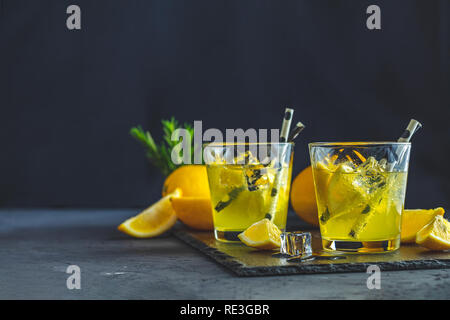 Lemon alcohol drink cocktail with ice, lemon and rosemary herb on black stone concrete surface. Traditional italian homemade lemon alcohol drink lique Stock Photo