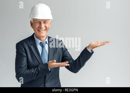 Professional Occupation. Constructor in hard hat standing isolated on gray showing space aside smiling happy Stock Photo
