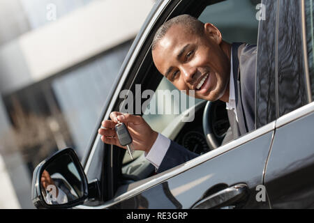 Young man sitting in new car looking out from window with key looking camera playful Stock Photo