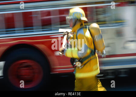 A fireman in full turnouts is carrying an axe at a fire site, USA Stock Photo