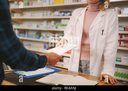 Customer handing over a medical prescription to the female chemist standing behind counter. Female apothecary taking prescription from customer at dru