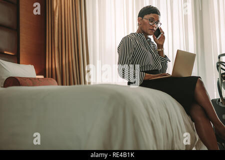 African businesswoman on tour working with laptop computer and mobile phone in hotel room. Female CEO on working from hotel room. Stock Photo