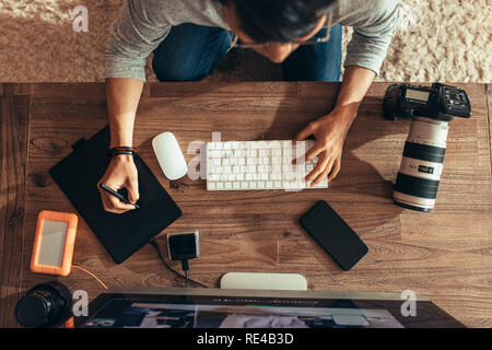 Top view of photographer editing photos after a photo shoot using graphic tablet and stylus pen. Photographer editing photos on desktop with camera an Stock Photo