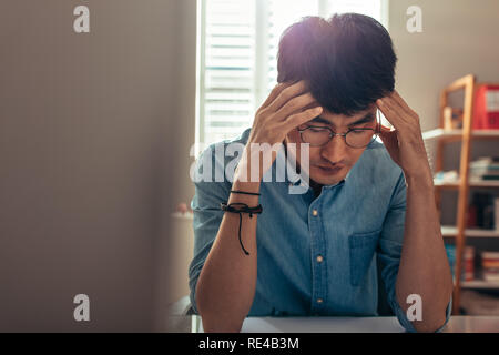 Man sitting at his desk looking stressed and tired. Man holding head in hands, looking stressed out because of failure. Stock Photo