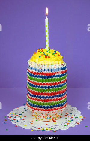 cupcake with polka dot candle in stack of colorful paper liners on white paper lace doily Stock Photo