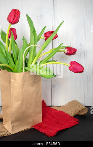 red tulips in generic paper bag on burlap fabric pieces with whitewashed wood background Stock Photo