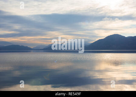 Sun  shining through clouds and mist with view of lake and mountains Stock Photo