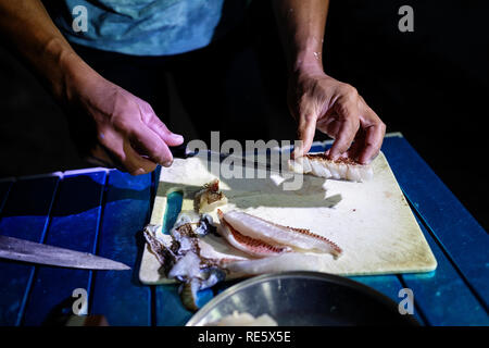 Close up of cooks hands slicing freshly caught fish for dinner on tropical beach, Iriomote, Japan Stock Photo