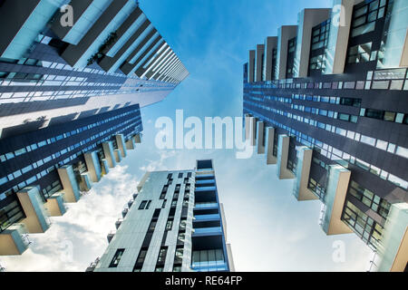 Low perspective view of modern Milan apartment blocks with large balconies looking up from below as they converge against a blue sky