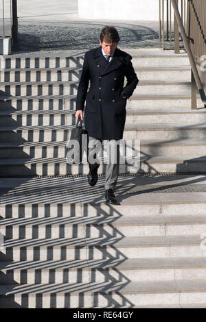 Businessman in coat walking down exterior concrete stairs with an interesting zigzag pattern from the shadow of the railing Stock Photo